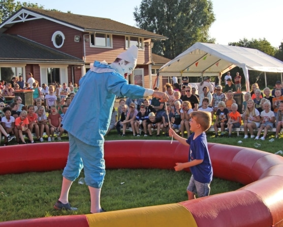 Clown maakt grapjes voor een kind in het midden van een cirkel, met andere kinderen op de achtergrond
